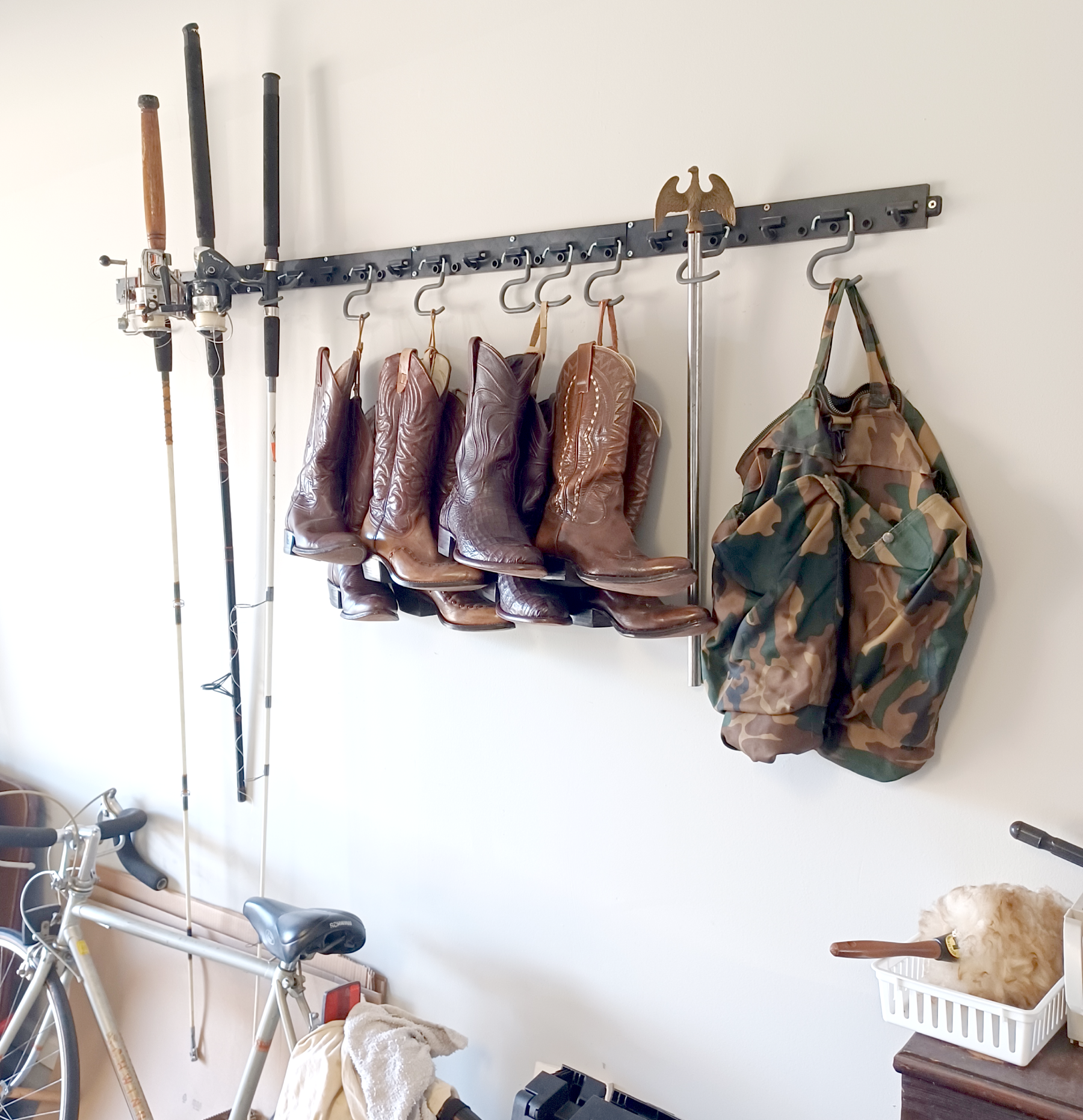 A rack holding fishing rods, bait, and a camouflage jacket on a white wall.