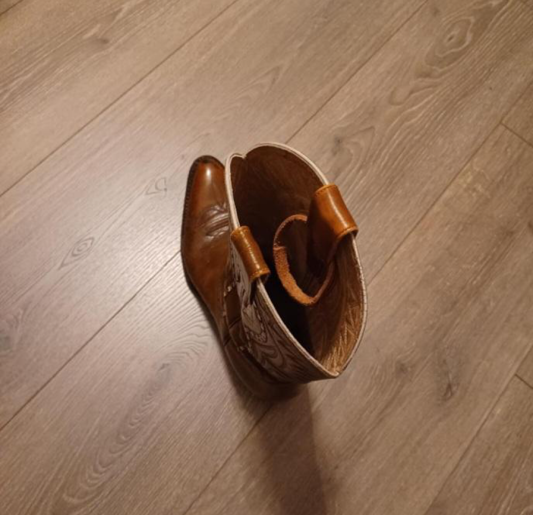 Brown leather cowboy boot on wooden floor.