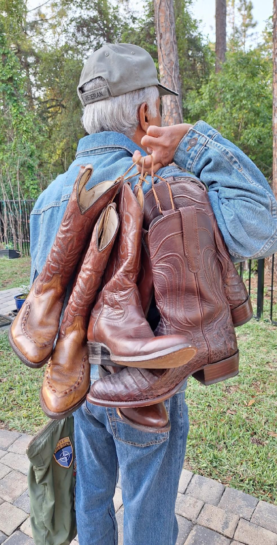 Man carrying multiple brown cowboy boots.