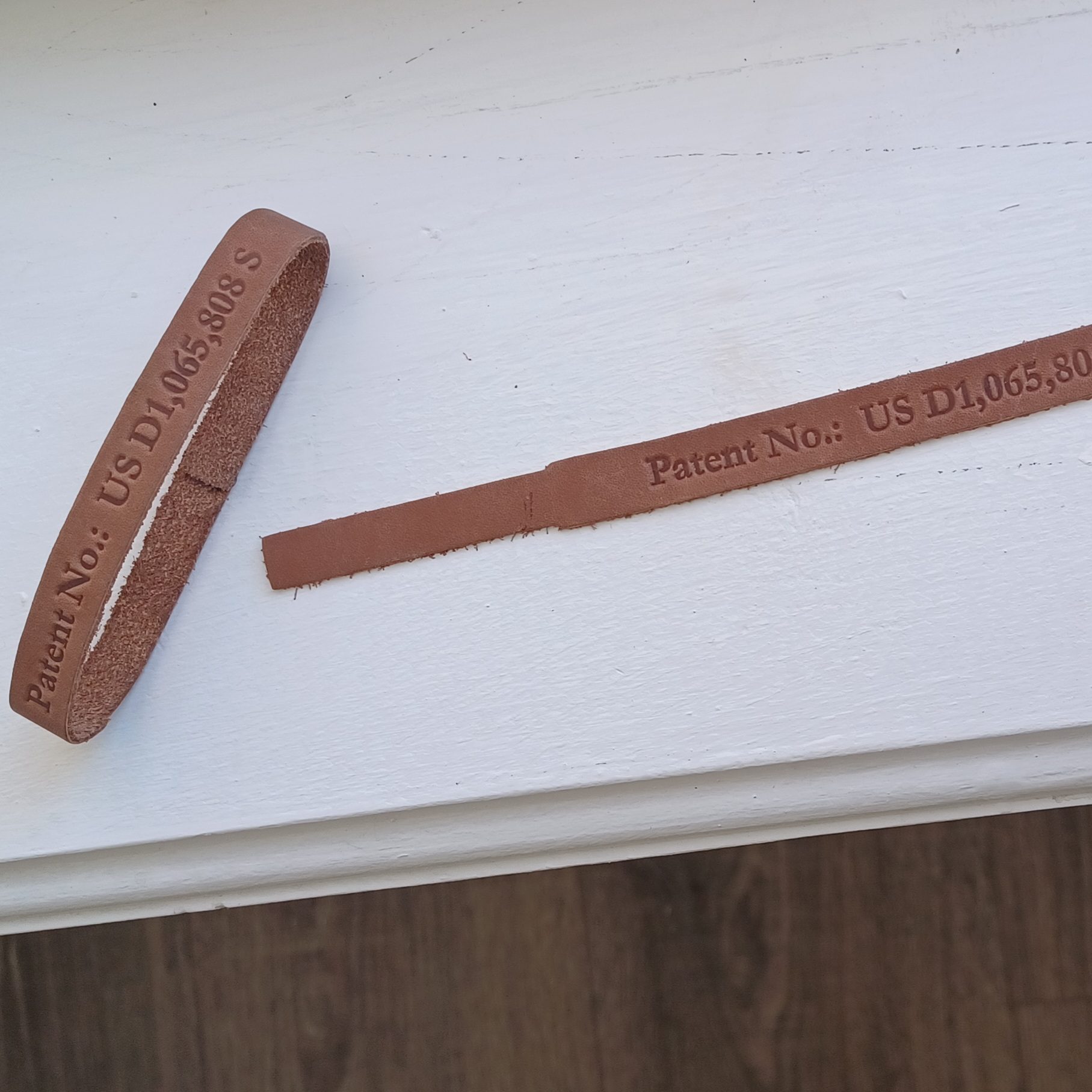 A brown leather belt with inscriptions lies on a white surface.
